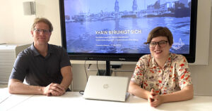 Felix Weisbrich, Leiter des Straßen- und Grünflächenamtes, und Stadträtin Annika Gerold sitzen an einem Tisch. Im Hintergrund ein Bildschirm mit einer Präsentation