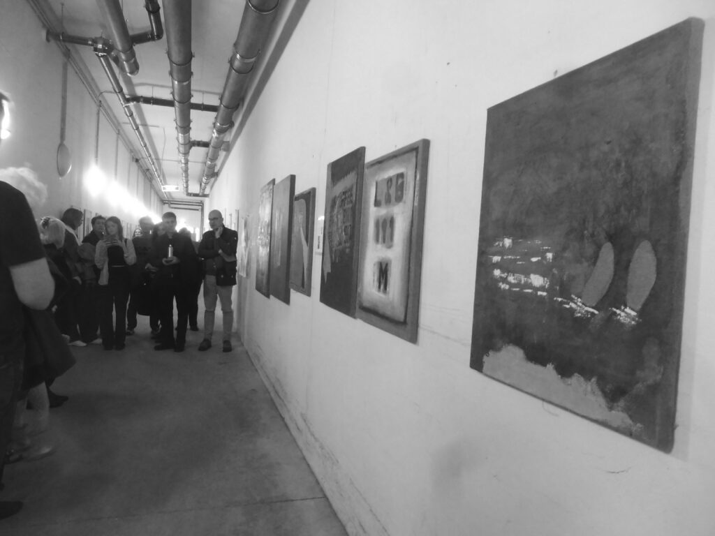 Besucherinnen und Besucher in einem Ausstellungsraum mit Gemälden und Fotografien an den Wänden.