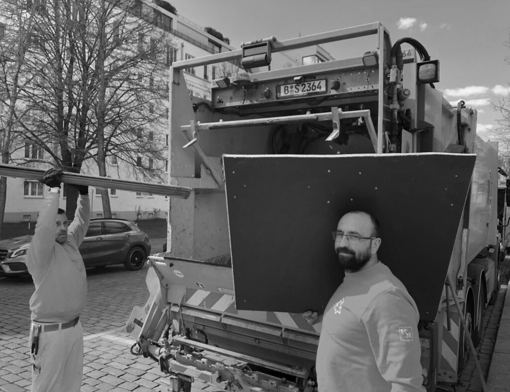 Zwei Personen laden einen großen Bildschirm an der geöffneten Rückseite eines BSR-Fahrzeugs ein.