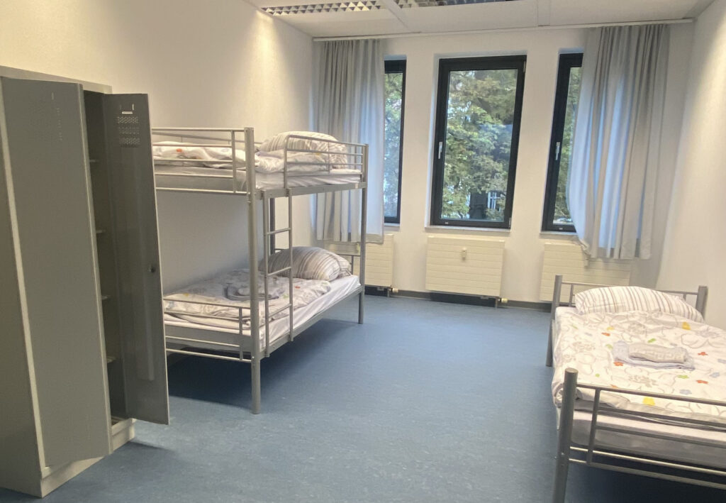 Mehrbettzimmer der Aufnahmeeinrichtung in der Hasenheide mit Etagenbetten, einem Einzelbett und Schränken.