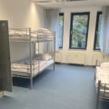 Mehrbettzimmer der Aufnahmeeinrichtung in der Hasenheide mit Etagenbetten, einem Einzelbett und Schränken.